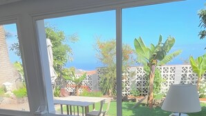 Ein Schlafzimmer mit großem Fenster, einem Bett, einem Tisch und einer Lampe.