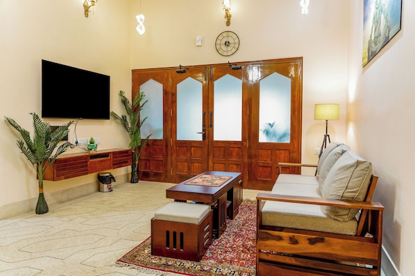 A living room with a flat-screen TV, wooden furniture, a patterned rug, and a large wooden door with frosted glass panels.