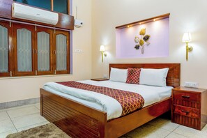 A hotel room with a wooden bed, a nightstand, a wall-mounted air conditioner, and a decorative wall piece.