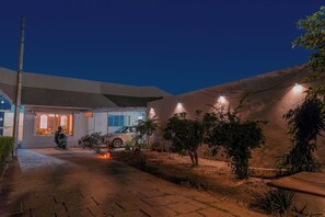 A residential property with a paved driveway, a parked scooter, and a car. There are potted plants and a small tree in the yard.