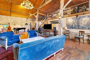 A rustic interior with a stone wall, wooden beams, a piano, blue upholstered furniture, and a large abstract painting. - Holiday Home 'Domaine Agenas' with Lake View, Private Pool and Wi-Fi (Monflanquin)