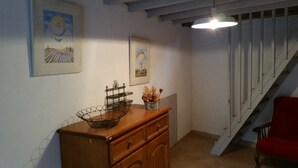 Een trap met een rode stoel, een houten kastje met een draadmand en twee ingelijste foto's aan de muur.