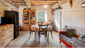 Een rustieke keuken met houten balken, een eettafel met stoelen, een koelkast en een bank met een plaid.