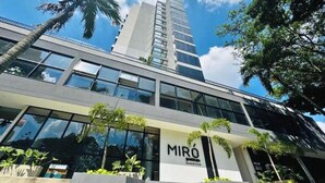 Un edificio moderno con fachada de vidrio, con el rótulo 'MIRÓ', rodeado de palmeras.