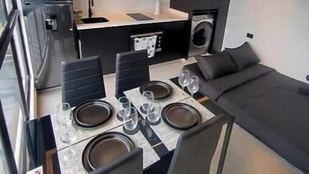 Una cocina compacta con electrodomésticos modernos, un comedor con una mesa preparada para cuatro personas y un sofá.