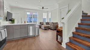 A modern kitchen with a central island, a dining area with a sofa, and a staircase with wooden steps. - Modern 3BR Waterfront Houseboat | Walk to Wilmington Riverwalk and Dining (Wilmington)