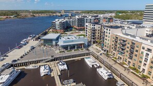 A marina with boats docked, a marina grill building, and modern apartment buildings. - Modern 3BR Waterfront Houseboat | Walk to Wilmington Riverwalk and Dining (Wilmington)