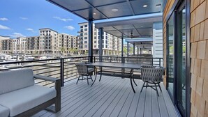 Una terraza cubierta al aire libre con asientos, vista hacia un puerto deportivo y edificios modernos al fondo.