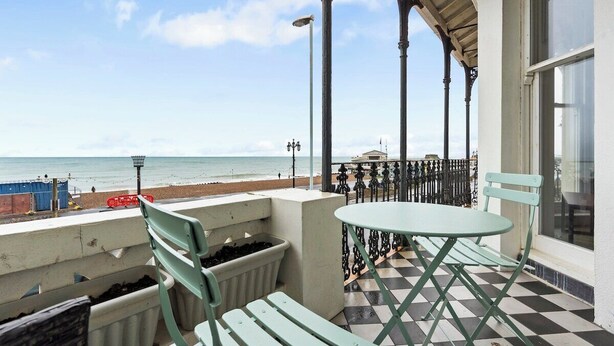 Eine Strandterrasse mit Tisch und Stühlen, Blick auf den Strand und ein Gebäude mit einem Balkon.