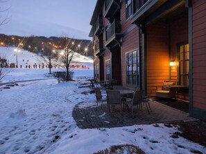 A building with a patio area, outdoor seating, and a view of a snowy landscape. - Amazing 1st floor Ski in/out Unit @ Creek (Vernon Township)