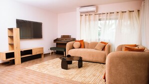 A living room with a sofa, a coffee table, a piano, and a TV on the wall.