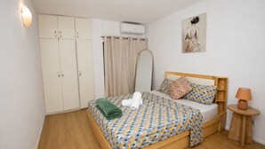 A bedroom with a bed, a wardrobe, a mirror, a painting, and a lamp.
