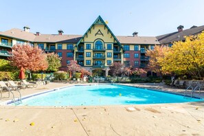 Ein Hotel mit Schwimmbecken, ein großes Gebäude mit markantem, dreieckigem Dach und herbstlich gefärbten Bäumen.