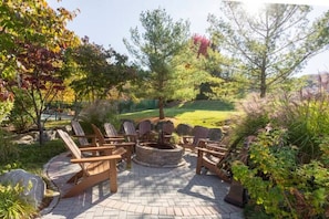 Eine Terrasse mit Adirondack-Stühlen, einem Steinkamin und einem angelegten Garten.