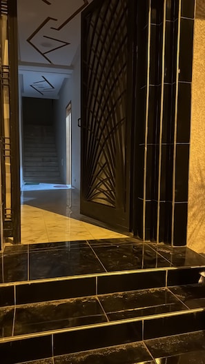 Um corredor com uma porta preta, escada e piso revestido de azulejos.