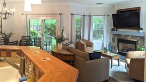 Una sala de estar con chimenea, televisor y comedor con barra.