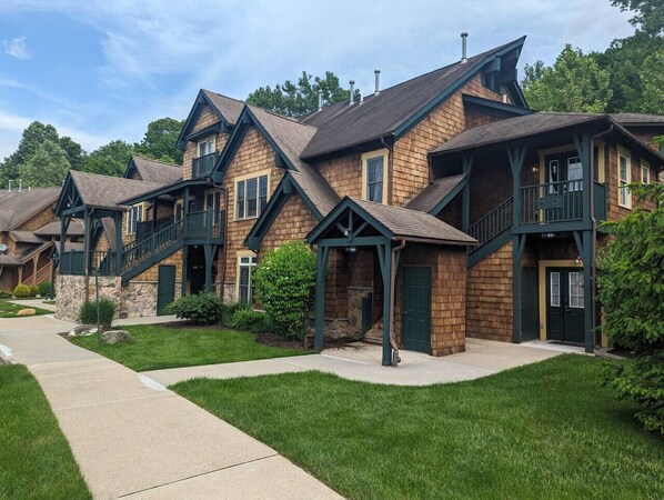 A row of wooden houses with green accents, a stone foundation, and a well-maintained lawn.