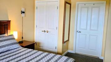 A hotel room with a bed, two white doors, a nightstand, a lamp, and a mirror.