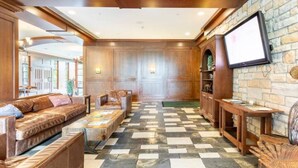 A spacious lobby with a checkered floor, wooden furniture, a television, and a stone wall.