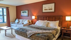 Quarto de hotel com uma cama grande, um sofá, uma mesinha e duas luminárias de cabeceira.