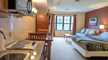 Une chambre d’hôtel compacte comprenant un coin cuisine, un lit, une petite table et une fenêtre avec des rideaux.