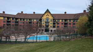 Um hotel com vários andares, piscina, cerca verde e árvores ao redor.