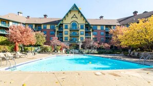 A hotel with a swimming pool, a large building with a distinctive triangular roof, and a landscaped area with trees.