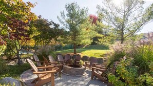 A patio with Adirondack chairs, a stone fire pit, and a landscaped garden.