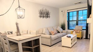 A living room with a sofa, a coffee table, and a dining table with chairs. - Renovated 1 Bedroom Valley View (Vernon Township)
