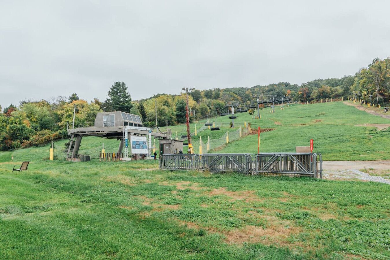 A grassy field with a small building structure, a fenced area, and a hilly background.