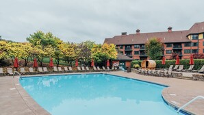 A swimming pool with lounge chairs and umbrellas, surrounded by trees and a building with multiple windows. - Renovated 1 Bedroom Valley View (Vernon Township)