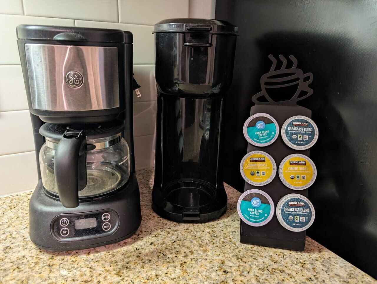 Une machine à café, une cafetière et un support à dosettes de café, avec différentes dosettes de café, sur un plan de travail de cuisine.