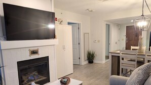 A living room with a fireplace, a flat-screen TV, a sofa, and a dining area. - Renovated 1 Bedroom Valley View (Vernon Township)