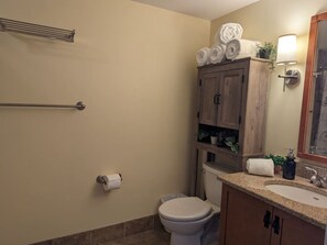 A bathroom with a toilet, sink, towel rack, and wooden cabinets.