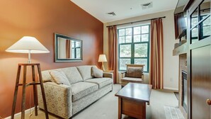 A living room with a sofa, a coffee table, a chair, a lamp, a fireplace, and a window with curtains. - RARE 1st flr Private Ski in/out access 1 Bed! (Vernon Township)