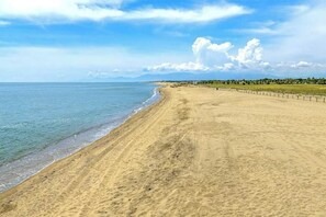 A wide sandy beach with gentle waves, a clear sky, and distant mountains. - Family mobile home Camping 5* Le Marisol (Torreilles)