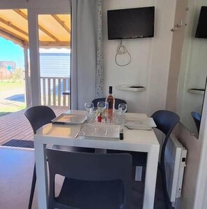 A dining area with a table set for two, a bottle of wine, and a TV mounted on the wall. - Family mobile home Camping 5* Le Marisol (Torreilles)