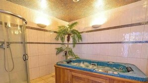 Ett badrum med en duschavdelning med glasväggar, ett träbadkar omgivet av blått mosaik och en palmplanta.
