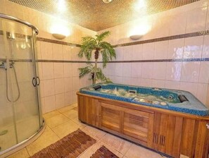 A bathroom with a glass shower enclosure, a wooden bathtub with a blue mosaic surround, and a palm plant. - Family mobile home Camping 5* Le Marisol (Torreilles)