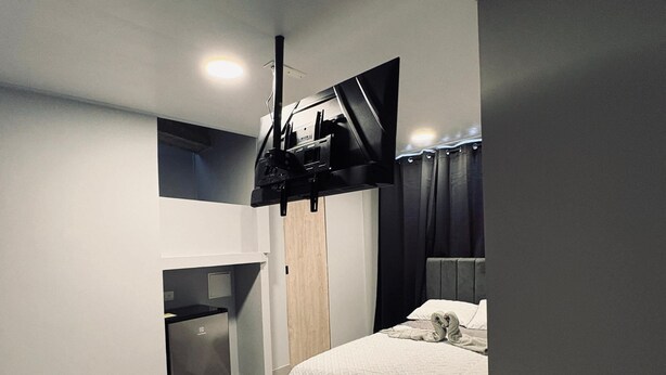 A bedroom with a bed, a TV mounted on the wall, a small kitchenette, and a ceiling light. - Central studio apartment in Santa Rosa De Cabal (Santa Rosa de Cabal)