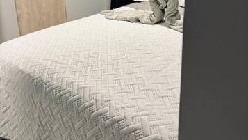 A bed with a white quilt, a wooden door, and a dark curtain.