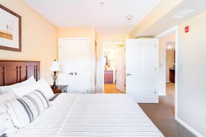 A hotel room with a large bed, a bedside table with a lamp, a framed picture on the wall, and a door leading to a bathroom.