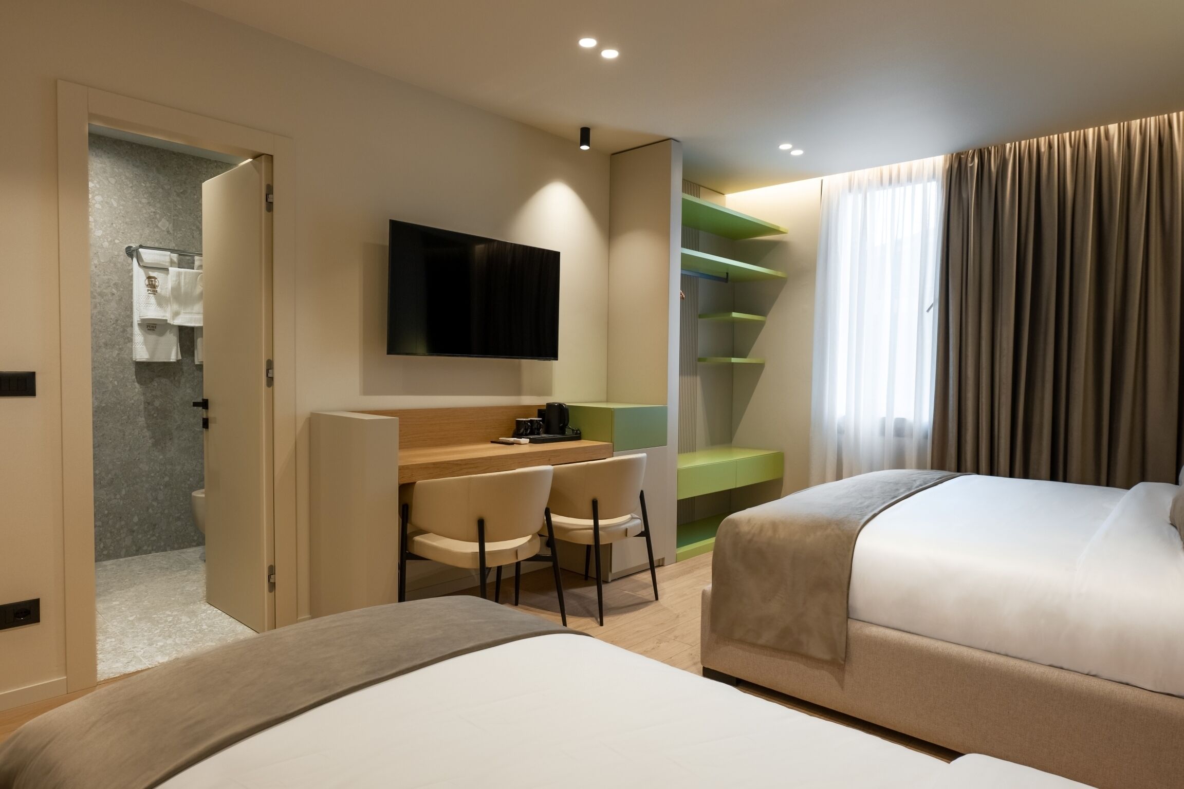 A hotel room with a bed, a desk with chairs, a television, and a staircase.
