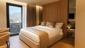A modern hotel room with a large bed, a desk with a telephone, and a view of the city through a large window. - Pusi Hotel (Tirana)