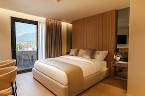 A modern hotel room with a large bed, a desk with a telephone, and a view of the city through a large window. - Pusi Hotel (Tirana)