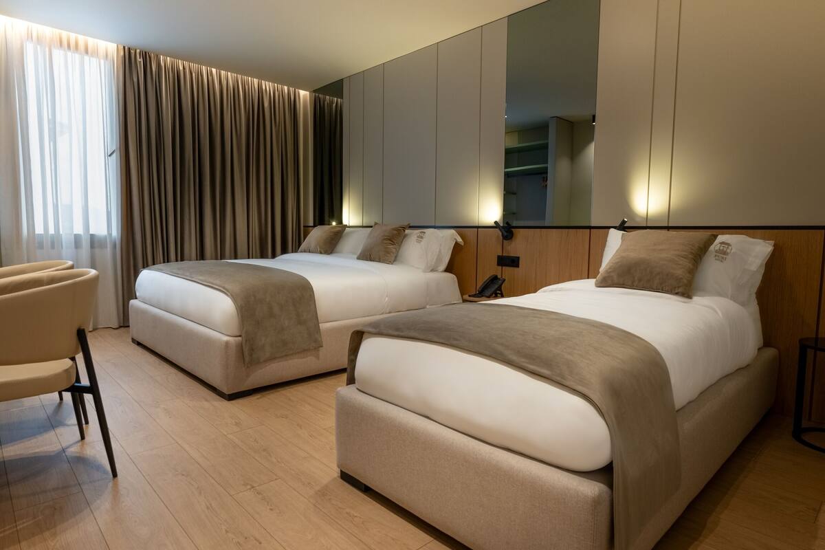 A hotel room with two beds, a chair, a mirror, and a wooden floor.