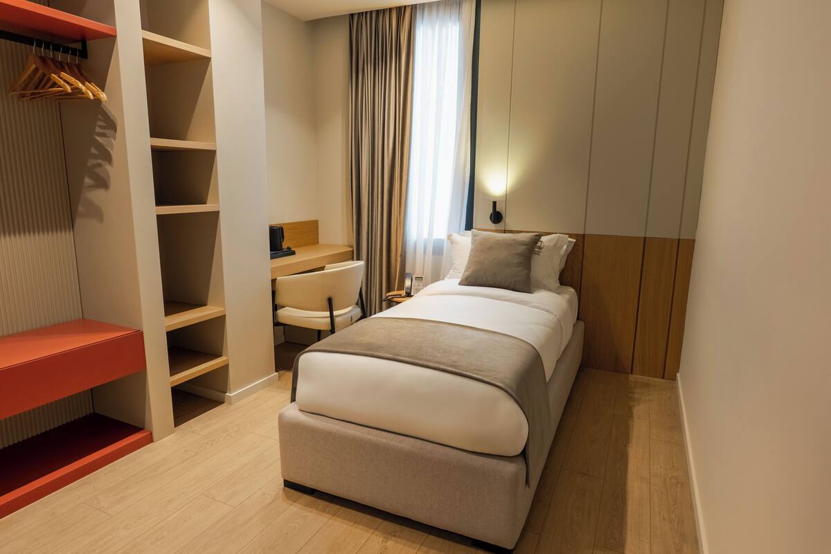 A bedroom with a bed, a desk, a chair, a wardrobe, and a hanging rack.