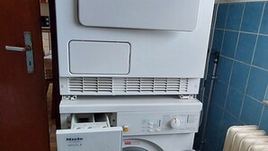 A large, white, two-door washing machine with a control panel and a dryer on top, located in a room with tiled flooring and a blue wall. - Haus Gloriosa: Where Black Forest tradition meets pure relaxation. (Bonndorf im Schwarzwald)