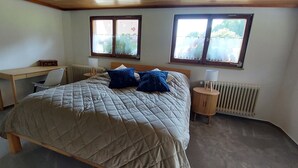 A bedroom with a bed, two windows, a desk, and a radiator. - Haus Gloriosa: Where Black Forest tradition meets pure relaxation. (Bonndorf im Schwarzwald)