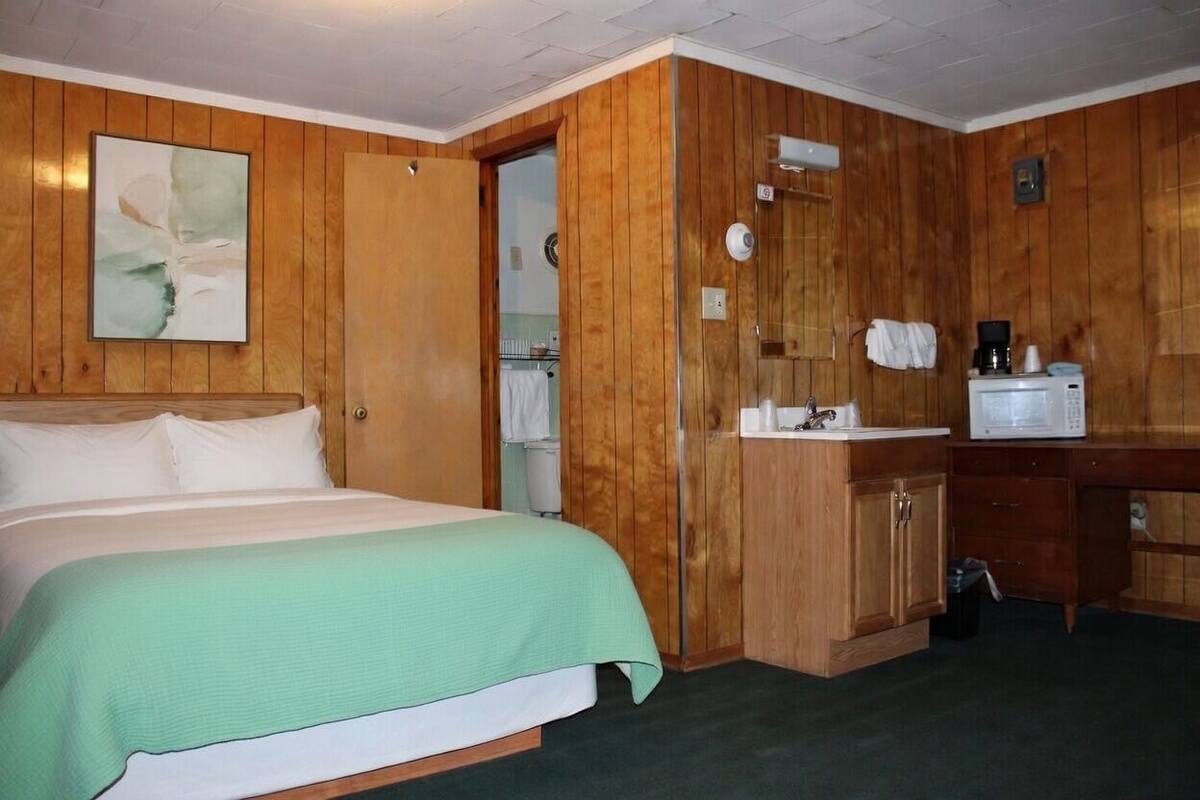 Habitación de hotel con cama, paredes de madera, una pequeña kitchenette y un cuadro en la pared.